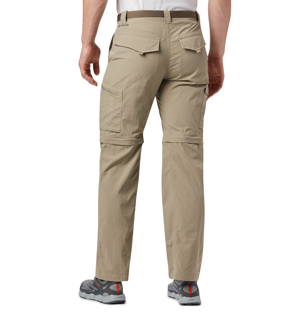 אדם לבוש במכנסי קולומביה IL Silver Ridge II Convertible, נעלי טיולים אפורות וחולצה לבנה עומד עם גבו אל הצופה. המכנסיים מצוידים ברוכסנים להפיכתם למכנסיים קצרים בברכיים, במספר כיסים, והם אידיאליים לפעילויות בחוץ.