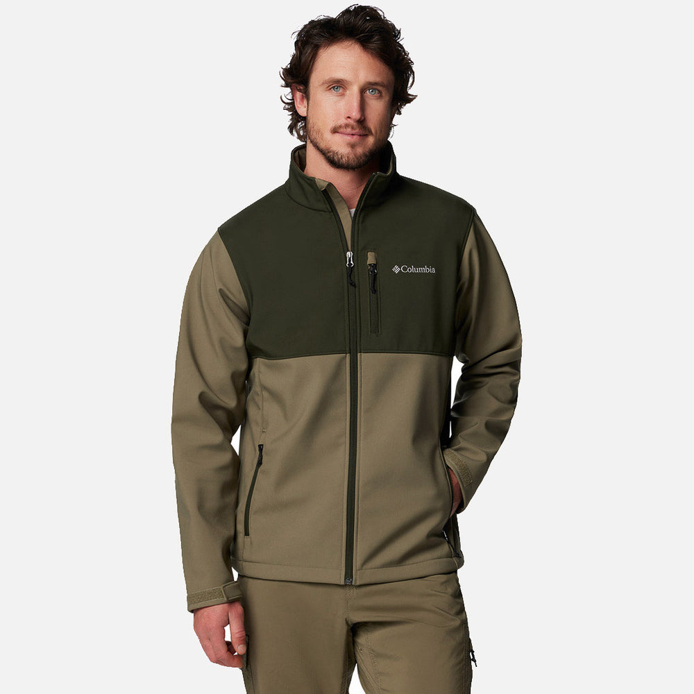 גבר לבוש במעיל Softshell של ColumbiaIL Ascender בצבעי זית וירוק כהה עומד, יד אחת בכיס, ומביט למצלמה על רקע לבן חלק.