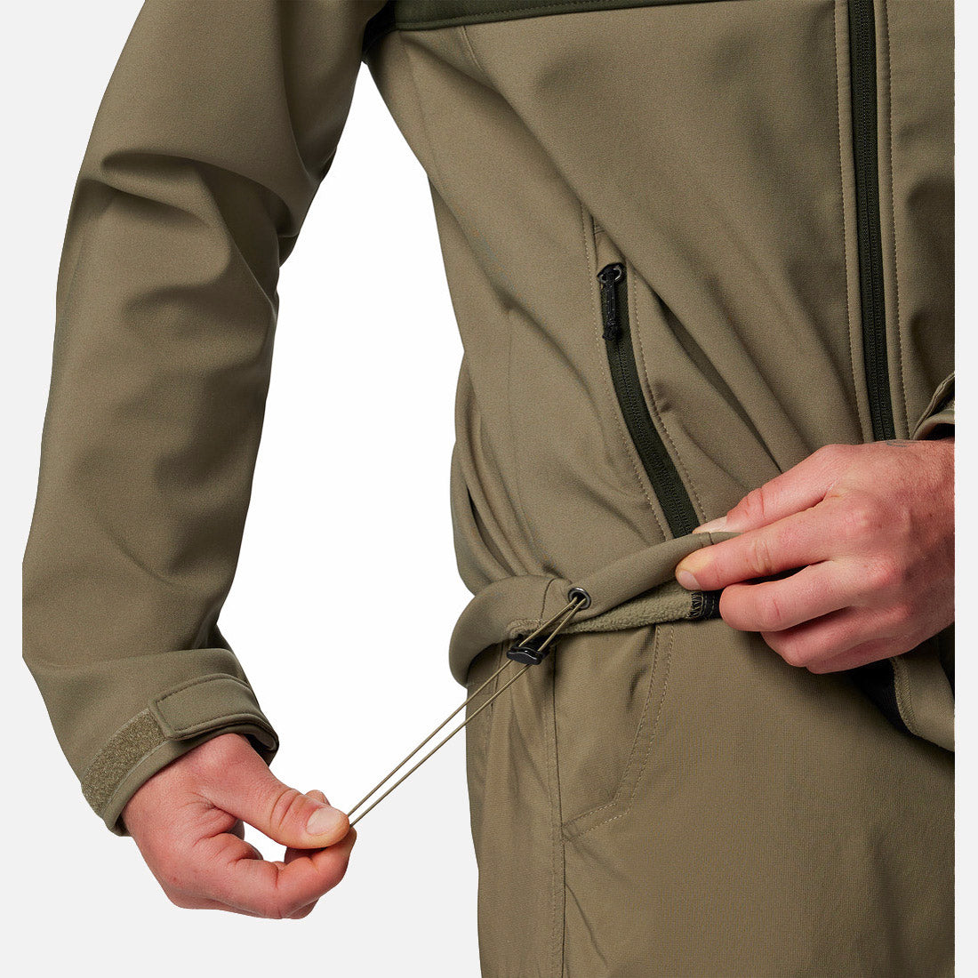 אדם מהדק את שרוך המותניים של מעיל ה-Ascender Softshell של ColumbiaIL בצבע ירוק זית, כשהוא מושך בידו הימנית תוך שהוא אוחז בבד בידו השמאלית; נראים רק פלג גופו העליון וידיו.