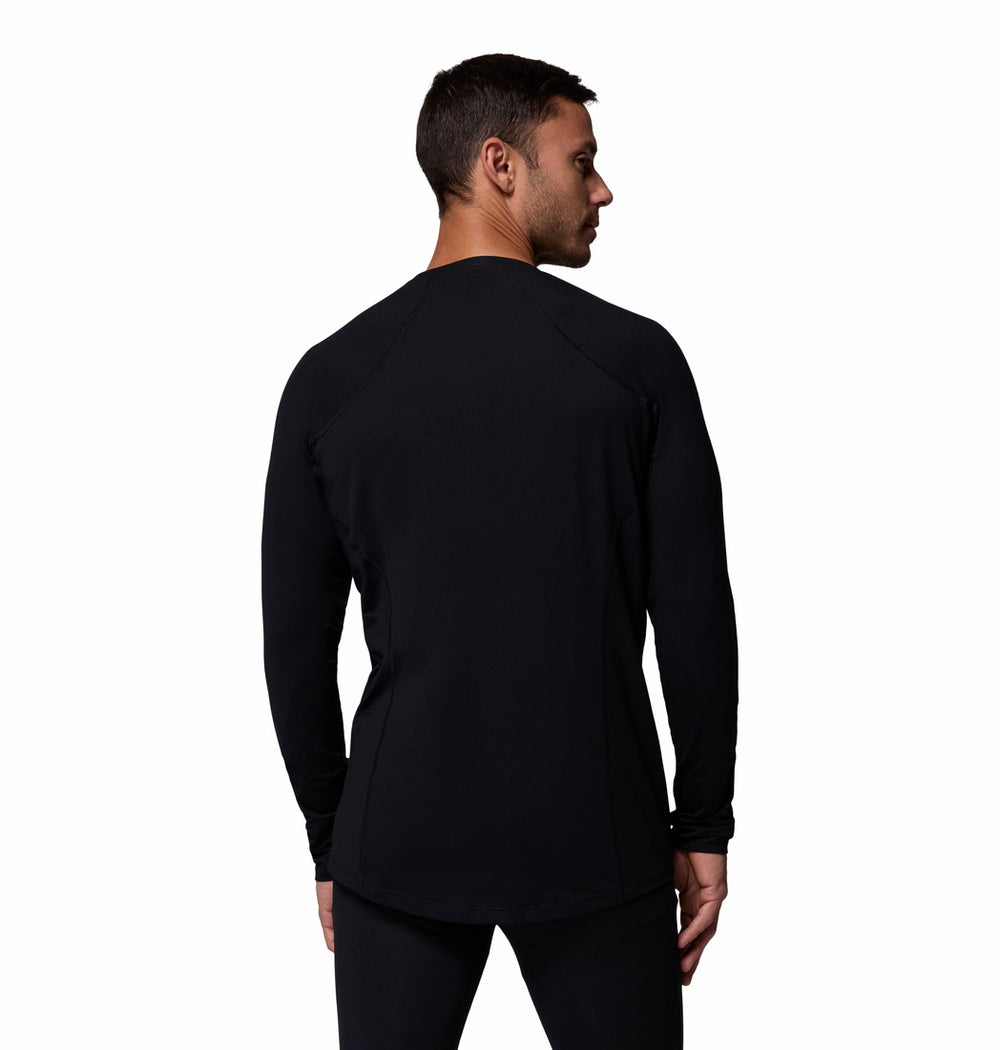 גבר לבוש בחולצת קולומביה IL Midweight Stretch Long Sleeve בצבע שחור, עם מכנסיים תואמים, עומד על רקע לבן חלק ומביט מעבר לכתפו השמאלית.
