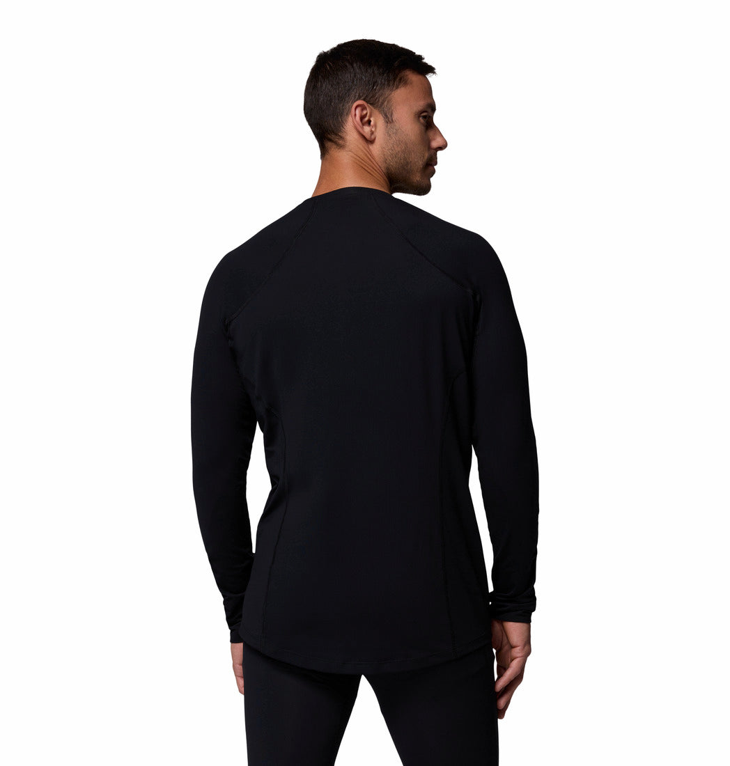 גבר לבוש בחולצת קולומביה IL Midweight Stretch Long Sleeve בצבע שחור, עם מכנסיים תואמים, עומד על רקע לבן חלק ומביט מעבר לכתפו השמאלית.