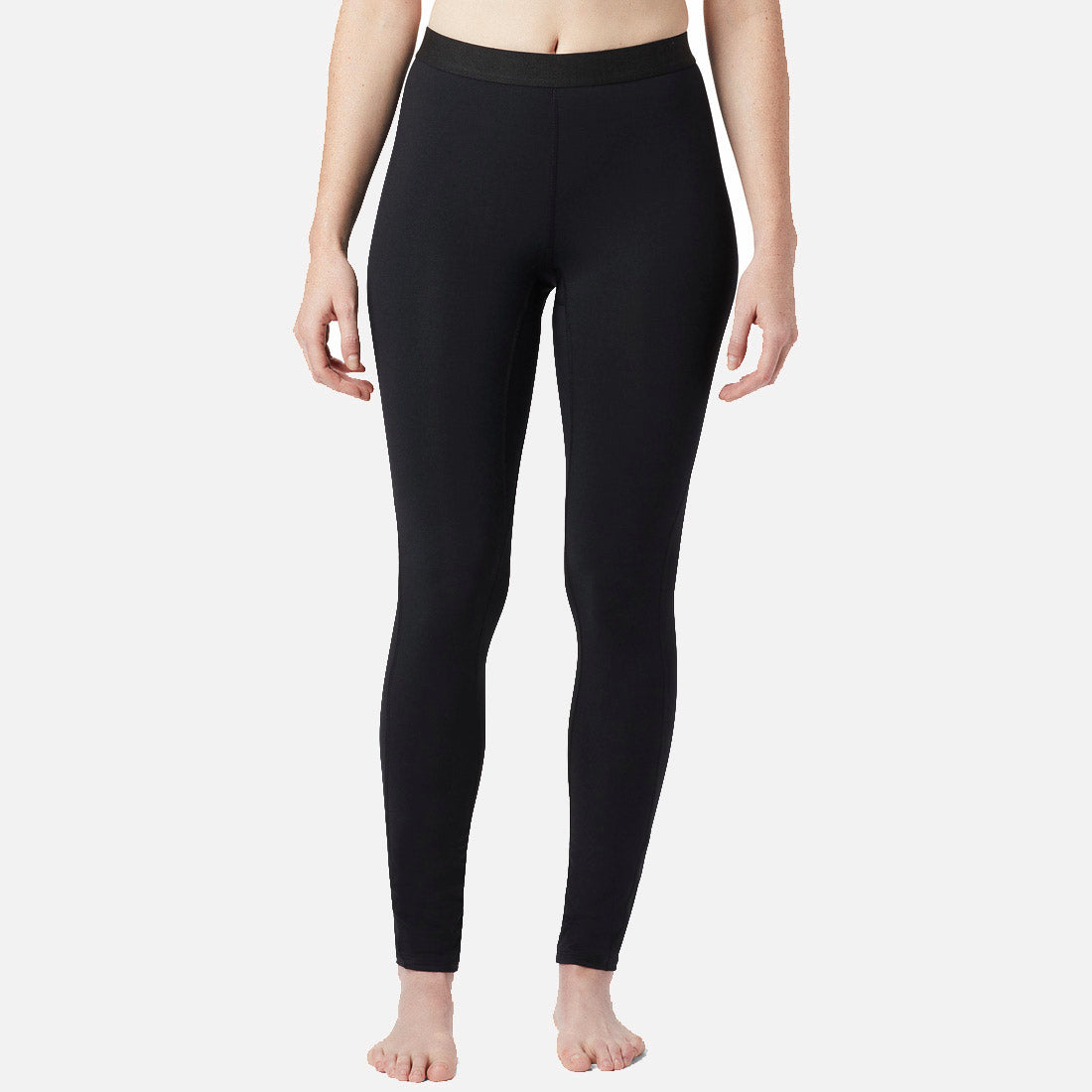 אישה עומדת יחפה על רקע לבן חלק, לבושה ב-Midweight Stretch Baselayer של columbiaIL — טייץ שחור באורך מלא עם מותן גבוהה. זרועותיה מונחות בנינוחות לצדי גופה; פלג גופה העליון נחתך בתמונה כדי להדגיש את הסגנון הקלאסי של בגדי הספורט לנשים.