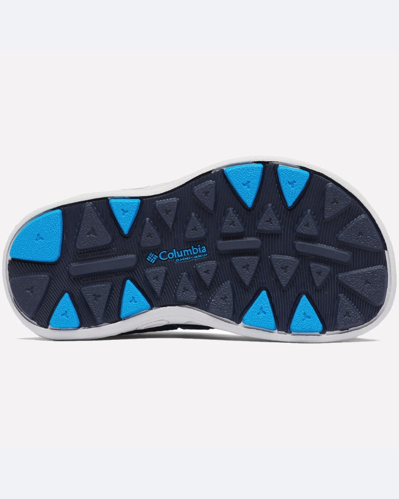 בתמונה נראית הסוליה של נעל הילדים "Techsun Wave" של קולומביה IL, עם חריצים משולשים בצבעי כחול ואפור כהה, המעניקים אחיזה. הלוגו של קולומביה IL המופיע במרכז מדגיש את העיצוב שלה כנעלי קיץ אידיאליות לילדים.