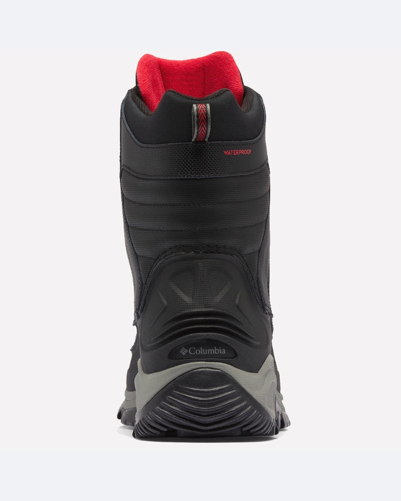 מבט מאחור על מגף חורף Bugaboot III של ColumbiaIL בצבע שחור עם נגיעות אפורות ואדומות, סוליה עבה עם חריצים, בטנה אדומה והכיתוב "WATERPROOF" בחלק העליון — אידיאלי לשמירה על יובש וחום בתנאי קור.