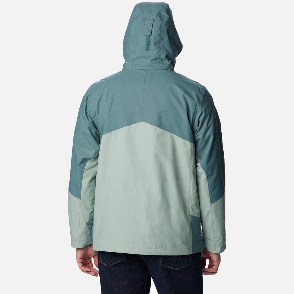 בתמונה נראה אדם מאחור, לבוש במעיל "Bugaboo II Fleece Interchange" של המותג columbiaIL בשני גוונים – טורקיז וירוק בהיר – כשהכובע מורם. עיצוב ה-INT עם בלוקי הצבע הזוויתיים מוסיף לו מגע מסוגנן.