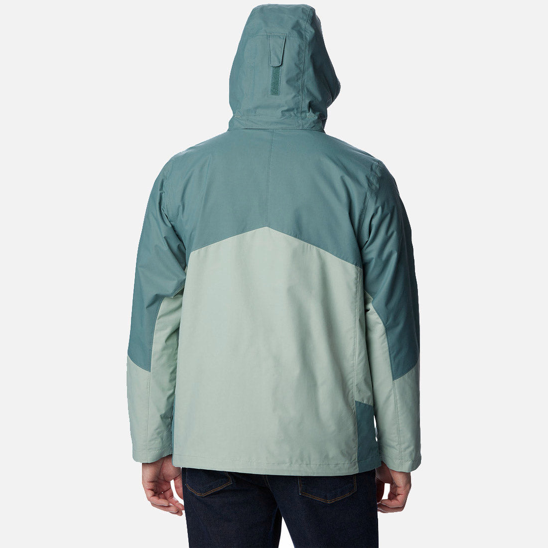 בתמונה נראה אדם מאחור, לבוש במעיל "Bugaboo II Fleece Interchange" של המותג columbiaIL בשני גוונים – טורקיז וירוק בהיר – כשהכובע מורם. עיצוב ה-INT עם בלוקי הצבע הזוויתיים מוסיף לו מגע מסוגנן.