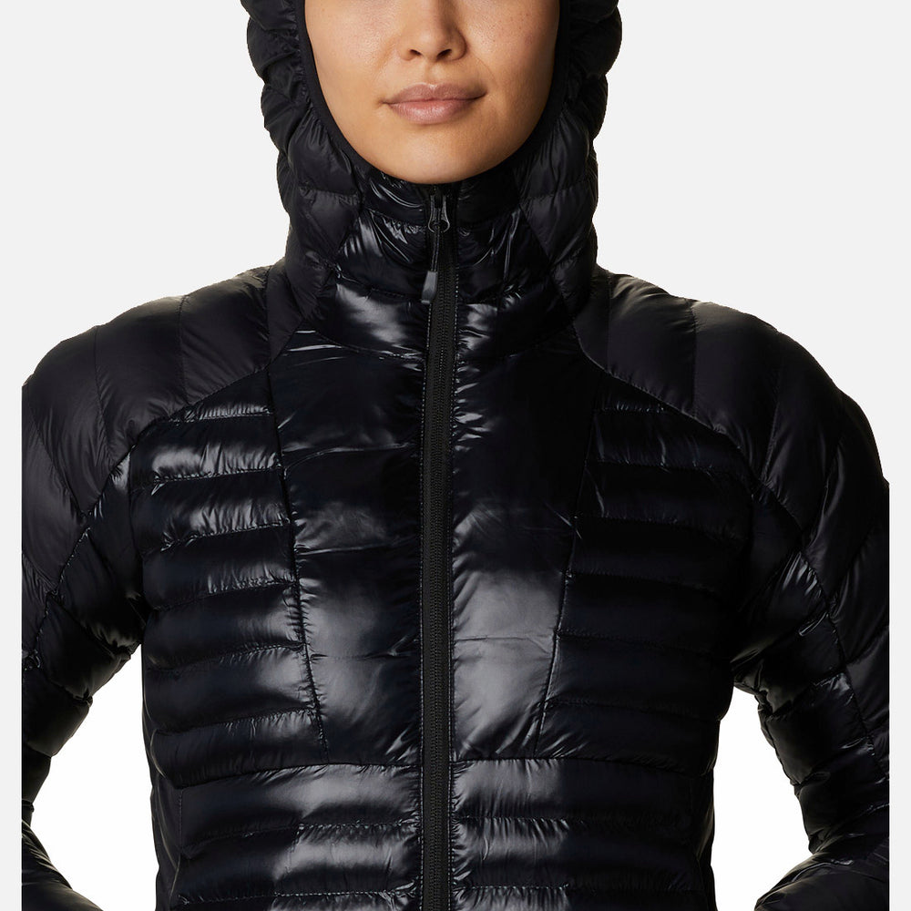 אישה לובשת את ColumbiaIL Labyrinth Loop Hooded W, מעיל פוך שחור ומבריק עם ברדס, כשהברדס מורם על רקע לבן — מושלם לשילוב עם נעלי נשים אלגנטיות מקולקציית LABYRINTH LOOP.