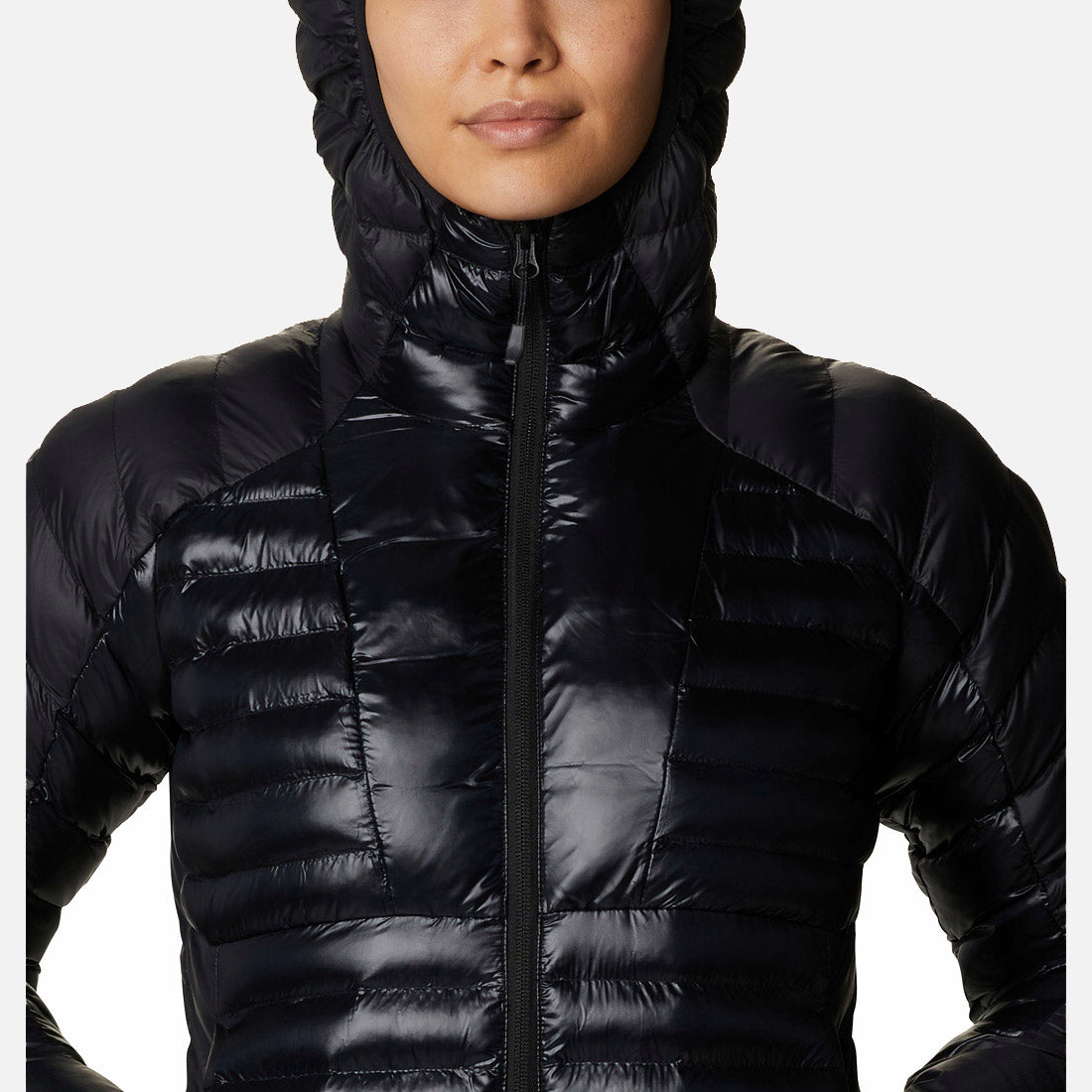 אישה לובשת את ColumbiaIL Labyrinth Loop Hooded W, מעיל פוך שחור ומבריק עם ברדס, כשהברדס מורם על רקע לבן — מושלם לשילוב עם נעלי נשים אלגנטיות מקולקציית LABYRINTH LOOP.
