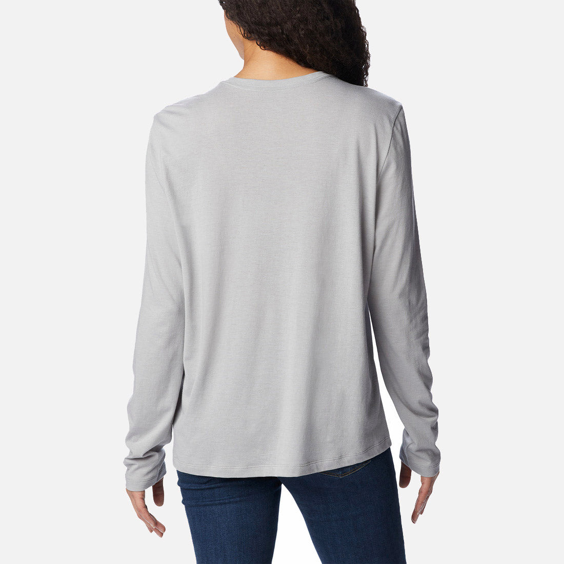 אדם בעל שיער ארוך ומתולתל, לבוש בחולצת Columbia Trek Relaxed L/S T מבית columbiaIL ובג'ינס כחול כהה, מצולם מאחור על רקע לבן חלק.