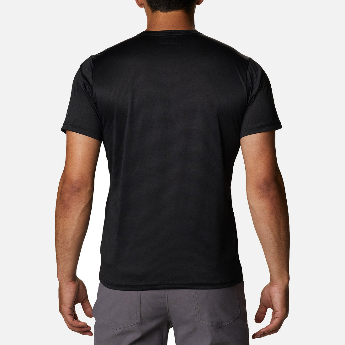A person is standing facing away from the camera, wearing a plain black Columbia hike crew t-shirt and gray pants, against a white background.