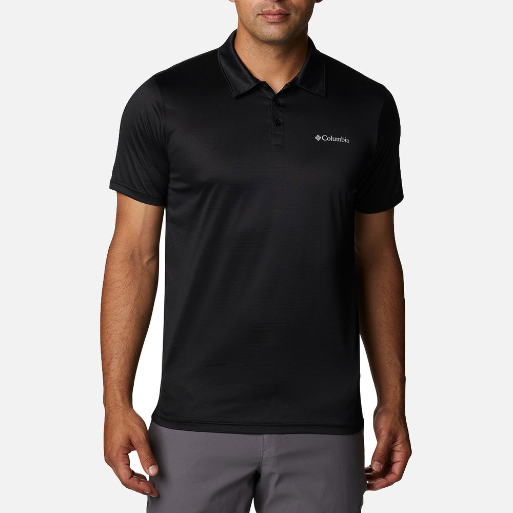 גבר לבוש בחולצת "Columbia Hike Polo Black" מבית columbiaIL, בעלת שרוולים קצרים, צווארון ושלושה כפתורים, בשילוב עם מכנסיים אפורים, עומד על רקע לבן חלק.