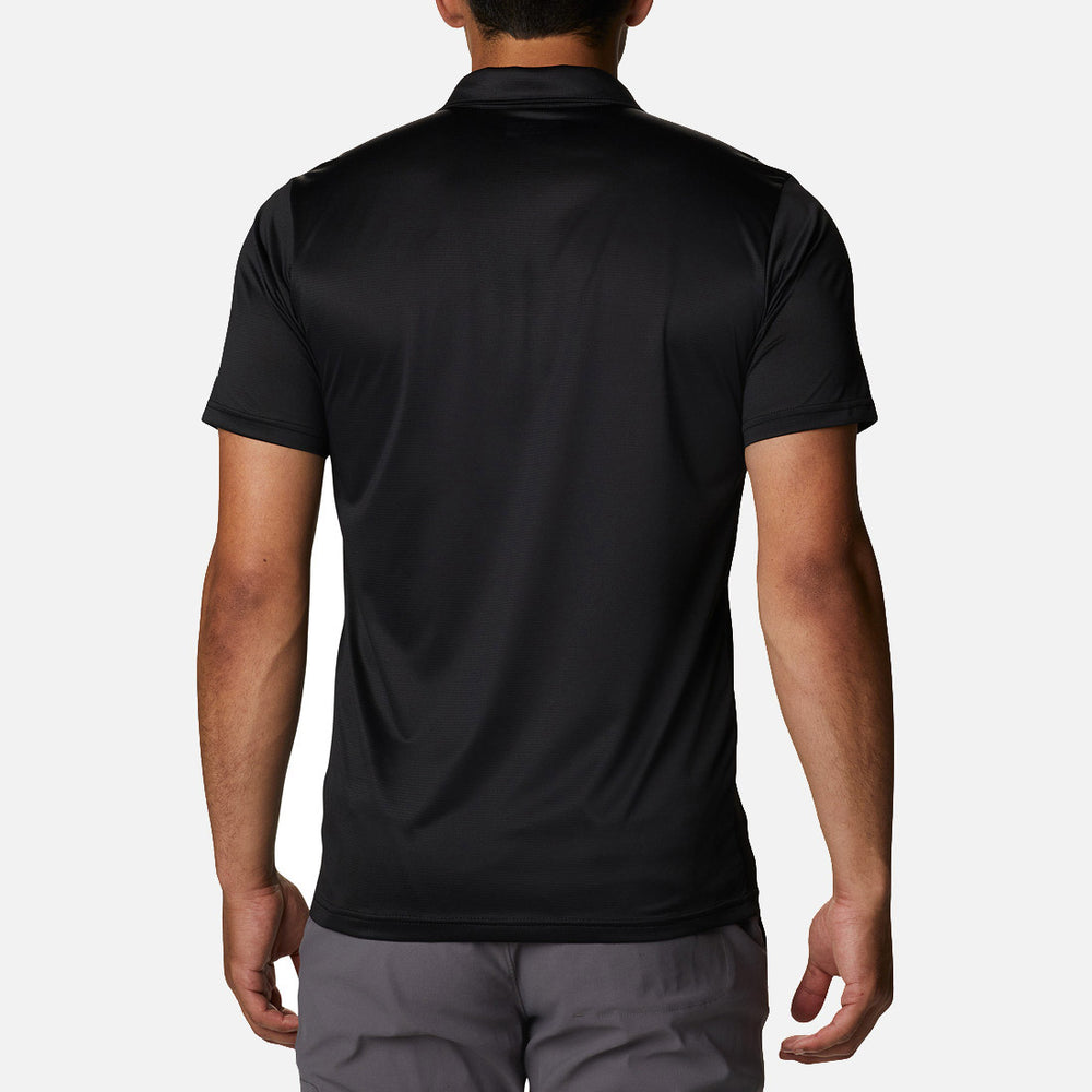בתמונה נראה גבר מאחור, לבוש בחולצת פולו "Columbia Hike Polo Black" של columbiaIL ובמכנסיים אפורים, עומד על רקע לבן חלק.