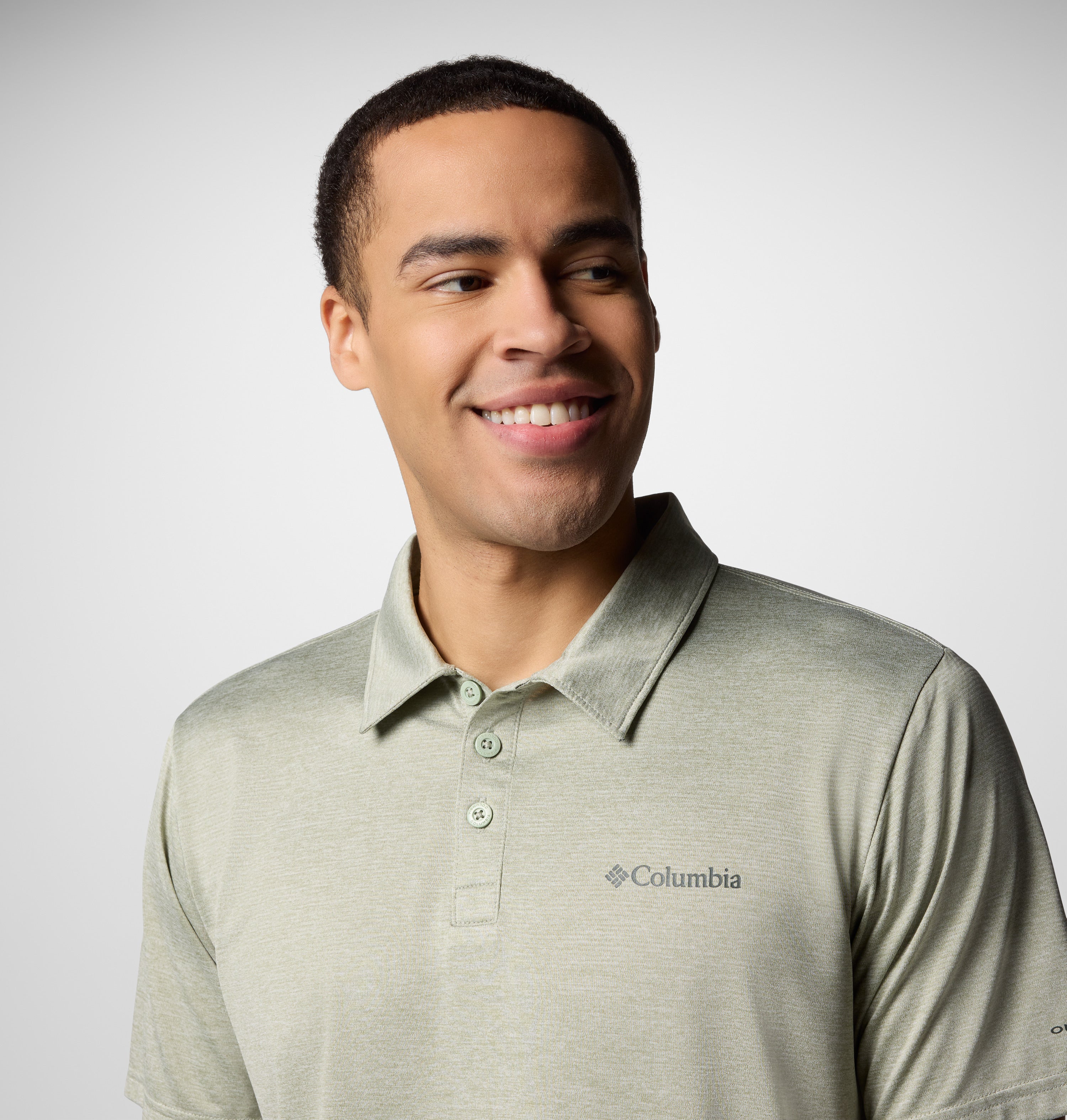 גבר לבוש בחולצת פולו "קולומביה ישראל Columbia Hike Polo" בצבע ירוק בהיר מחייך תוך שהוא מביט שמאלה, על רקע אפור בהיר אחיד.