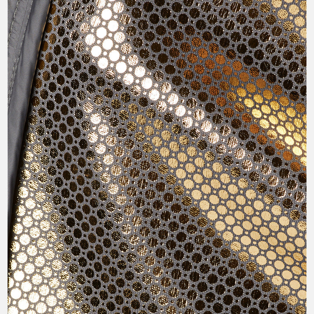 תקריב של בד ה-Softshell של ColumbiaIL Canyon Meadows: דוגמת רשת בצבעי זהב וכסף מטאליים עם חורים עגולים קטנים המרווחים באופן אחיד, המשקפים את האור ויוצרים אפקט מרקם ומנצנץ.