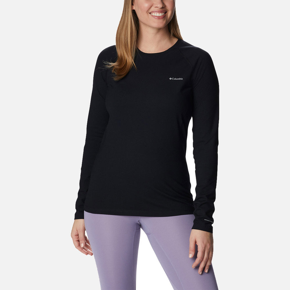אישה הלובשת חולצת קולומביה IL W Omni-Heat Infinity Knit L/S Crew ומכנסי טייץ סגולים בהירים עומדת ומחייכת על רקע לבן חלק.