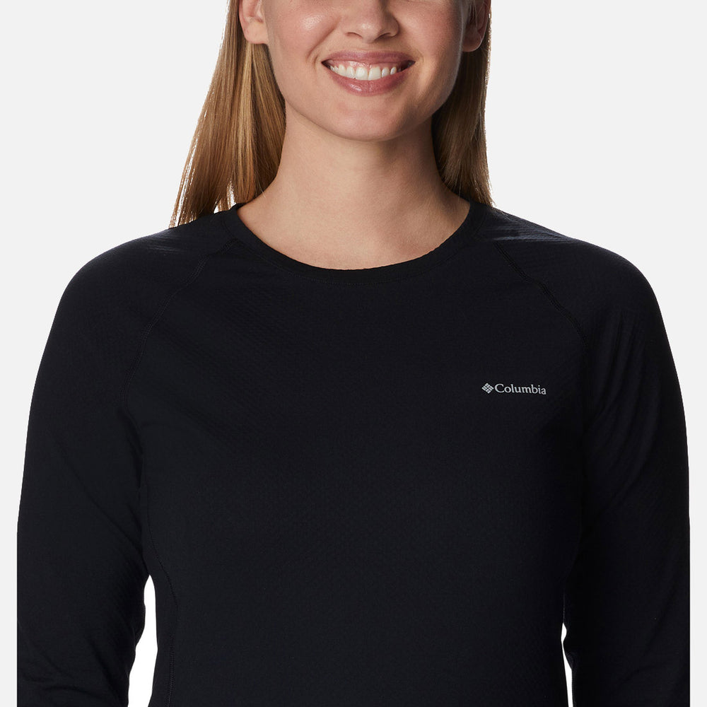 אישה בעלת שיער חום בהיר וישר מחייכת כשהיא לובשת את הסווטשירט "columbiaIL W Omni-Heat Infinity Knit L/S Crew" בצבע שחור, המוצג מהכתפיים ומעלה על רקע בהיר ופשוט.