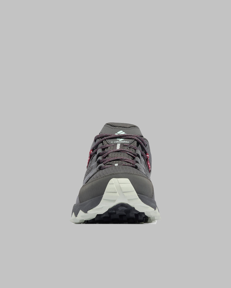 מבט מלפנים על נעל הטיולים Peakfreak Hera Outdry מבית קולומביה ישראל, בצבע אפור כהה עם שרוכים בשחור ולבן, סוליה אפור בהיר ודפוס מחוספס על רקע אפור בהיר אחיד — מושלמת להרפתקאות בטבע.