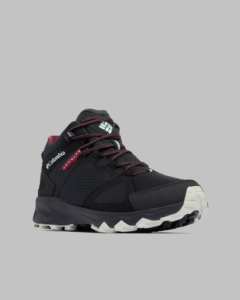 מגף טיולים יחיד מדגם Peakfreak Hera Mid Outdry מבית קולומביה ישראל, בצבעי שחור ואדום כהה, עם סוליה חיצונית לבנה ודפוס מחוספס, מוצג בזווית על רקע אפור בהיר. לוגו המותג הבולט מדגיש את העיצוב המותאם לפעילויות בשטח.