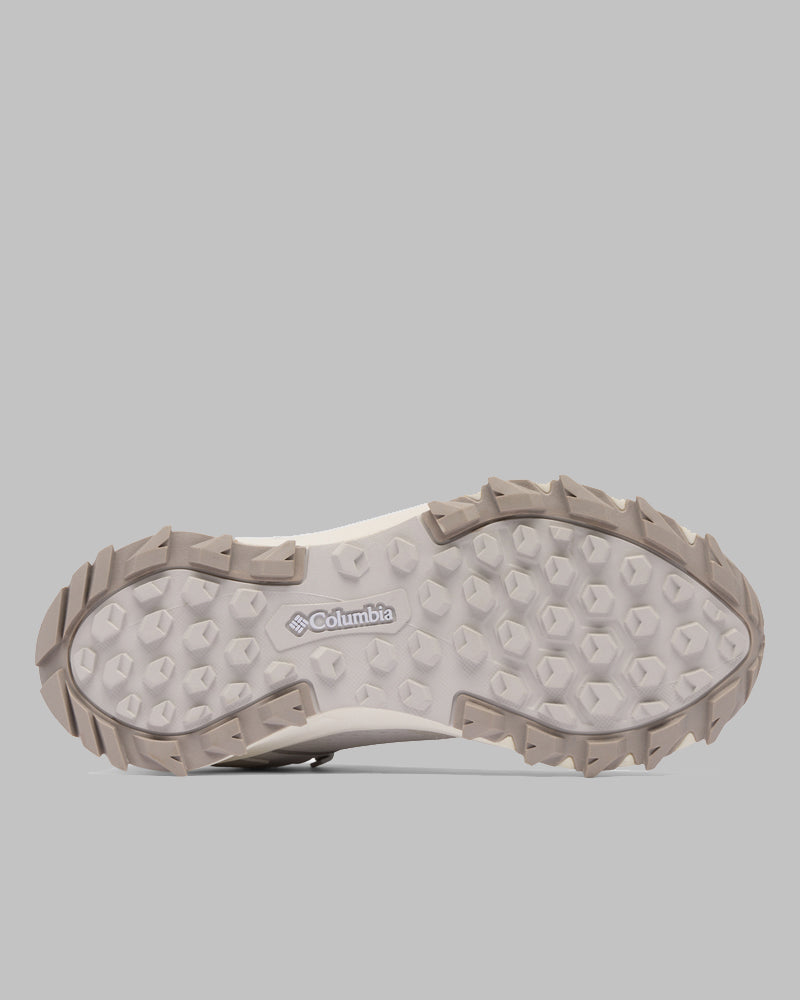 בתמונה נראית הסוליה של נעל ה-Peakfreak Hera Mid Outdry מבית קולומביה ישראל, הכוללת פרופיל סוליה בצבע אפור בהיר עם דפוסי אחיזה משושים וזוויתיים. לוגו קולומביה מופיע במרכז, על רקע אפור אחיד.
