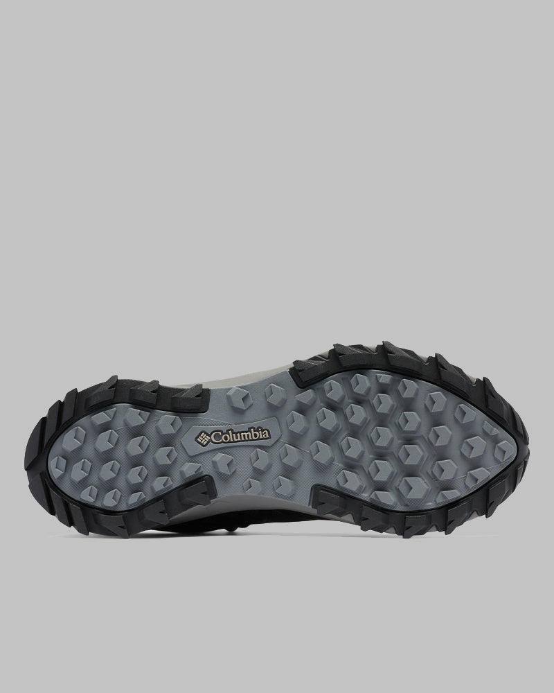 בתמונה נראית הסוליה של מגף הטיולים לגברים Peakfreak II Mid Outdry M מבית columbiaIL, הכוללת סוליה אפורה ומרקמת עם בליטות אחיזה שחורות ולוגו של קולומביה בקרבת המרכז. הרקע הוא אפור בהיר אחיד.