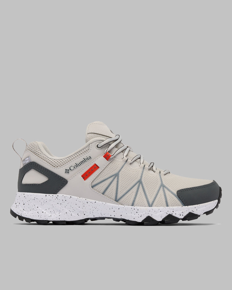 נעלי ריצת שטח מדגם Columbia Peakfreak II Outdry בצבעי בז' ואפור, עם דוגמאות גיאומטריות, נגיעות כתומות, סוליה אמצעית לבנה מנוקדת, סוליה חיצונית שחורה ושרוכים אפורים, מוצגות על רקע אפור אחיד.