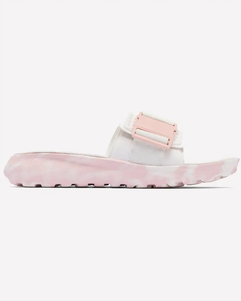 ה-Peakfreak Roam Slide של ColumbiaIL היא סנדל נשים לבן עם רצועה עבה, אבזם ורוד גדול וסוליה ורודה בהירה עם מרקם, המוצג בפרופיל על רקע לבן אחיד.