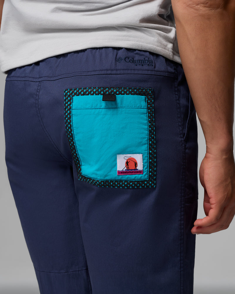 אדם הלובש מכנסיים קצרים "Bonefish Flats" של קולומביה ישראל בצבע כחול כהה, עם כיס טלאי בצבע טורקיז בגב, לוגו צבעוני ושוליים מנוקדים בשחור. נראים רק החלק התחתון של הגב וחלק מזרוע אחת.