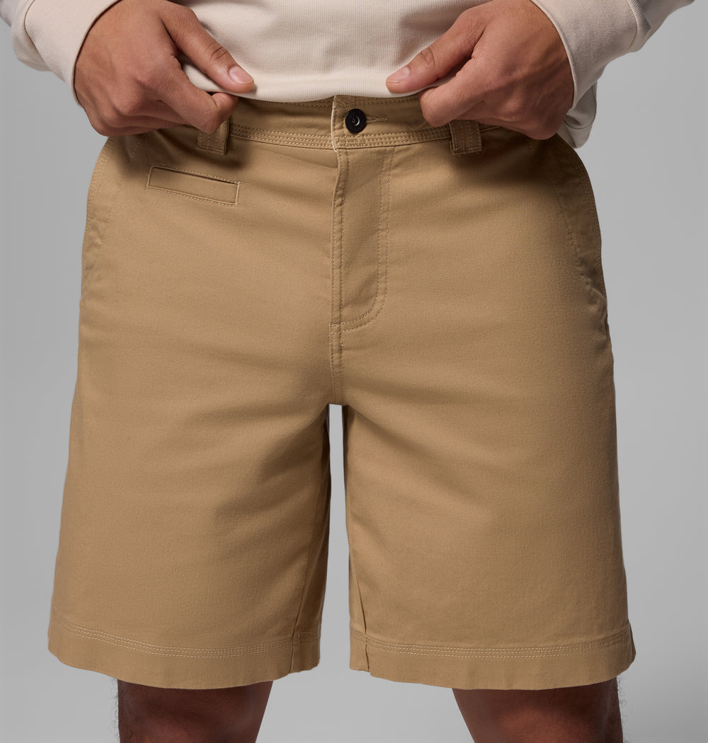 אדם לבוש במכנסיים קצרים מדגם "Acker Rock Twill" של קולומביה ישראל ובחולצה בצבע בז' בהיר עם שרוולים ארוכים עומד כש ידיו מונחות ליד חגורת המכנסיים על רקע אפור, ומדגיש את הרב-תכליתיות של בגדי החוץ.