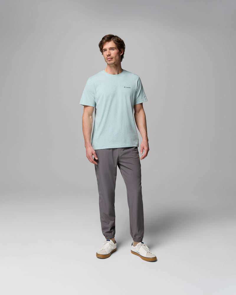 גבר עומד באולפן, לבוש במכנסיים אפורים מדגם Vital Valley Jogger של קולומביה ישראל, חולצת טי-שירט בצבע תכלת ונעלי ספורט לבנות. יש לו שיער קצר, והוא מביט מעט הצידה בהבעה ניטרלית על רקע אפור אחיד.