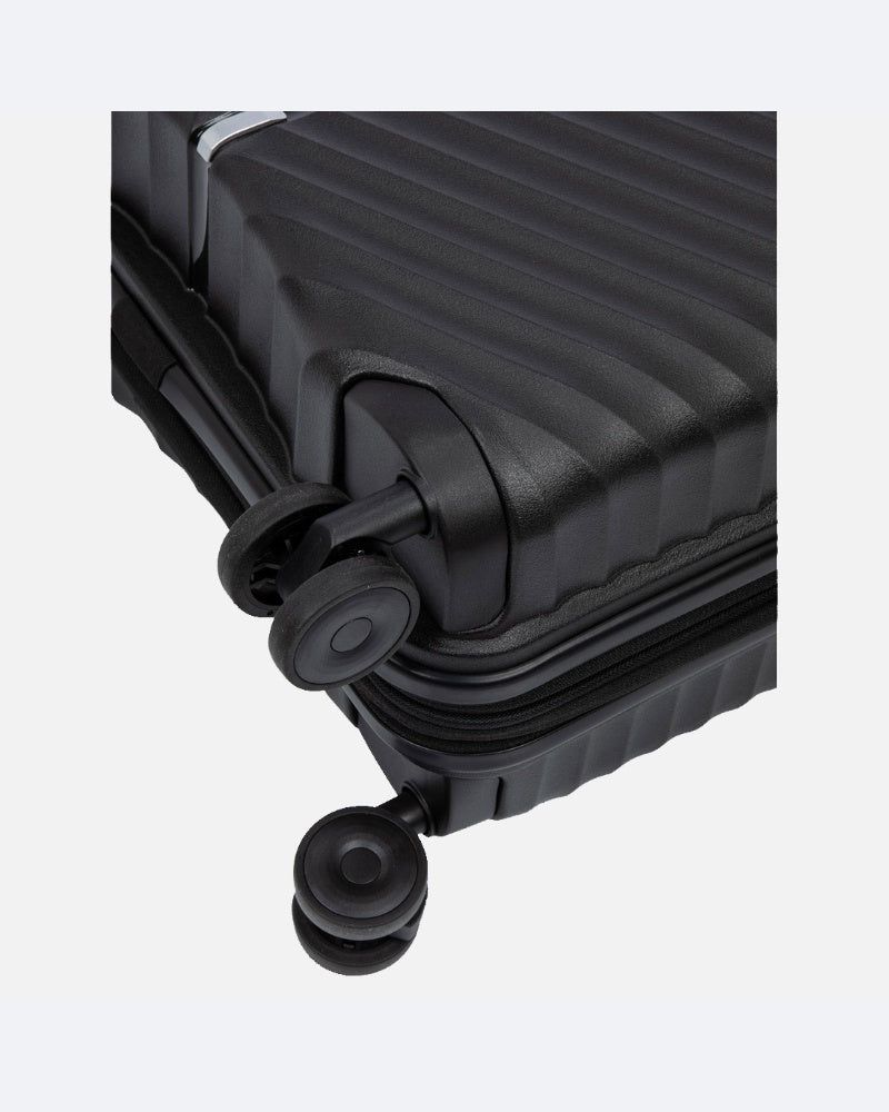 תקריב של פינת מזוודה קשיחה מדגם "Oakland Black" של חברת ColumbiaIL, בעלת משטח מחורץ ומרקם ייחודי ושני גלגלים מסתובבים בצבע שחור, על רקע בהיר וחלק.