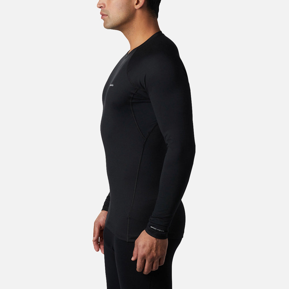 גבר עומד בפרופיל, לבוש בחולצת קולומביה IL Heavy Weight Stretch Long Sleeve Top בצבע שחור ובמכנסיים תואמים, על רקע בהיר וחלק, מוכן לאימון כוח או לכל שגרת כושר.