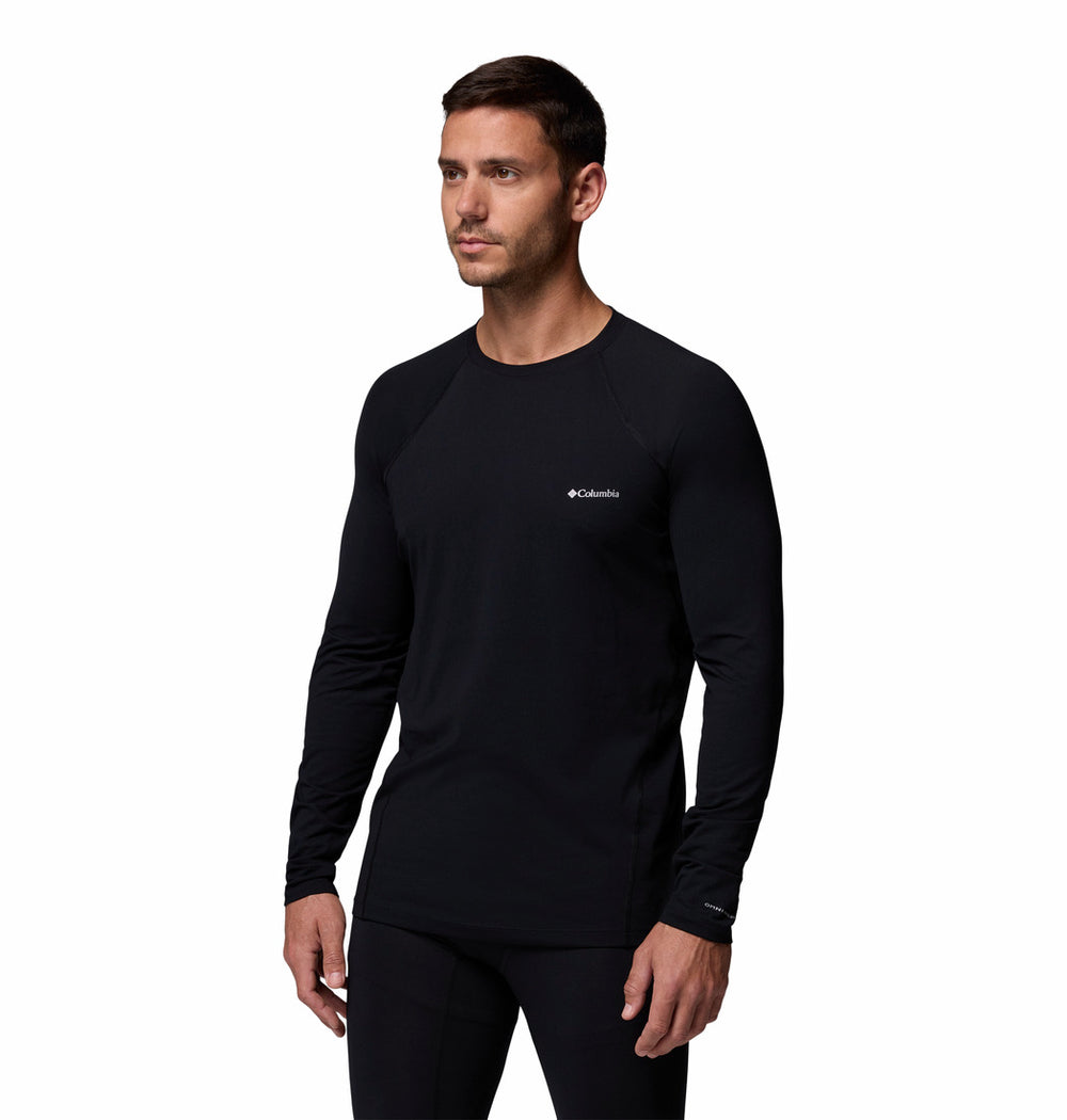 גבר עומד על רקע לבן, לבוש בחולצת קולומביה IL Midweight Stretch Long Sleeve Top בצבע שחור עם מכנסיים תואמים, ומביט מעט הצידה.