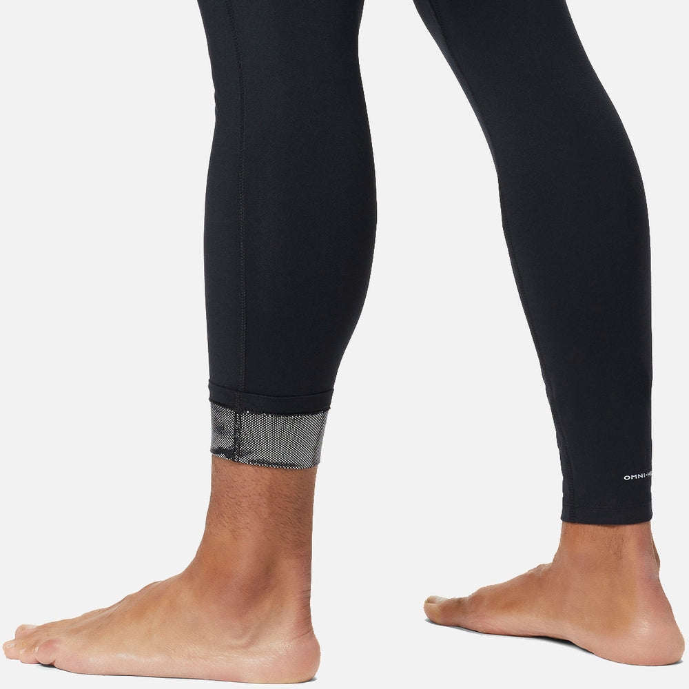 אדם לובש טייץ "Midweight Stretch Baselayer" של columbiaIL, עם פרט רשת בקרסול, ועומד יחף על רקע לבן.