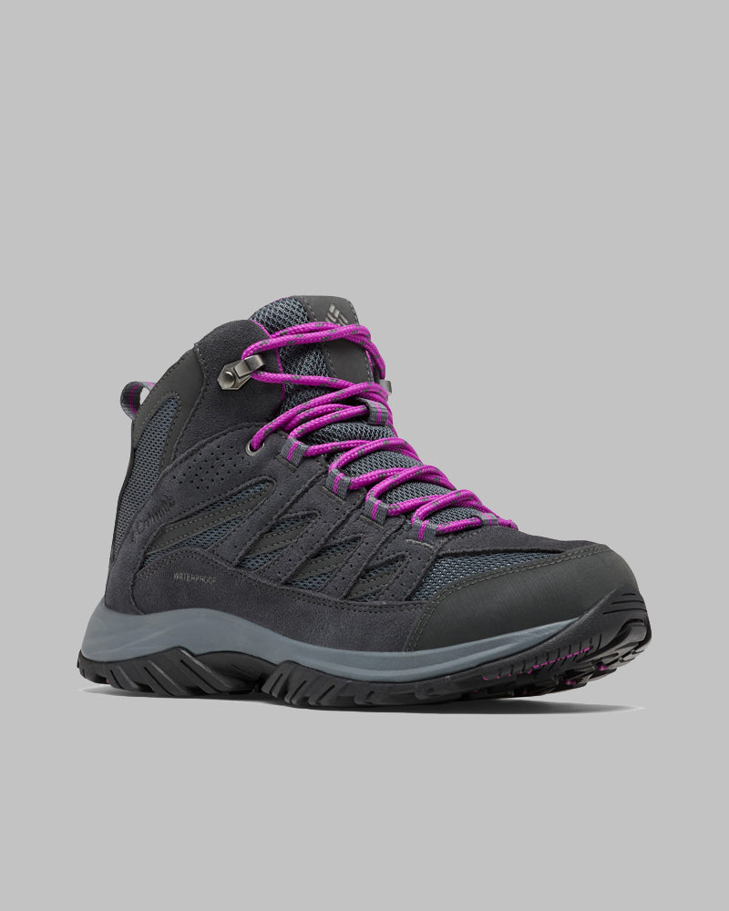 מגפי הנשים ColumbiaIL Crestwood Mid Waterproof W בצבע אפור כהה עם שרוכים סגולים, לוחות רשת וסוליה שחורה ועמידה מוצגים על רקע אפור בהיר — מושלמים כמגפי טיולים אטומים למים.