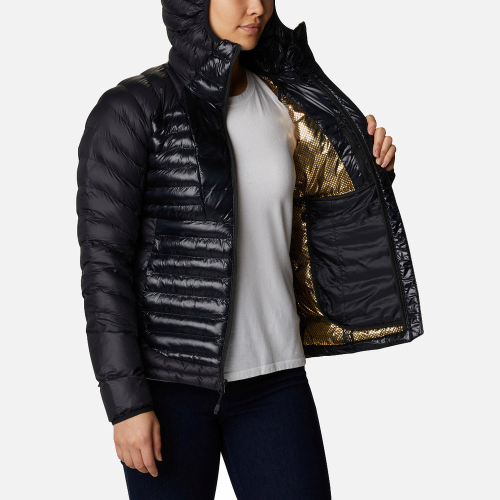 אדם לובש את מעיל הפוך עם קפוצ'ון "קולומביה IL Labyrinth Loop Hooded W" — מעיל פוך שחור עם קפוצ'ון, שנפתח חלקית כדי לחשוף את בטנתו המבריקה בצבעי זהב ושחור עם הכיתוב "LABYRINTH LOOP" ואת הכיס הפנימי הגדול — בשילוב עם חולצה לבנה, מכנסיים כהים ונעלי ספורט אלגנטיות.
