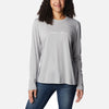 אישה לובשת חולצת Columbia Trek Relaxed L/S T מבית columbiaIL, עם הכיתוב "Columbia" באותיות כתב יד לבנות על החזה, יחד עם ג'ינס כחול כהה, כשהיא עומדת על רקע לבן חלק.