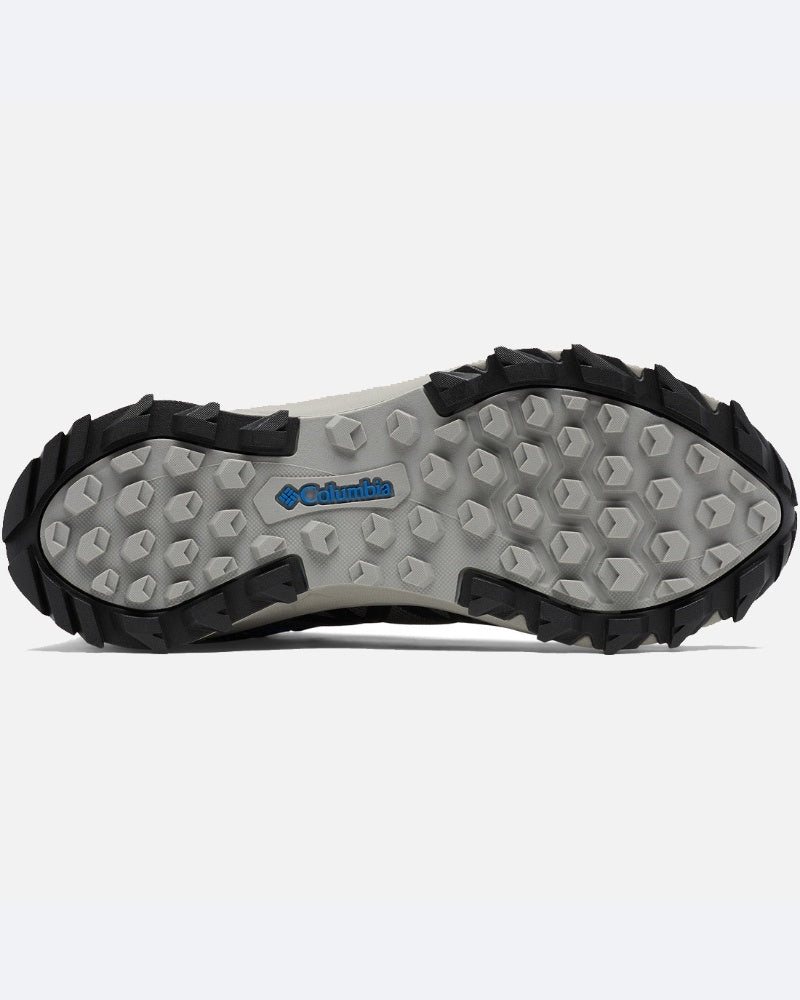 בתמונה נראית הסוליה של נעל ה-Peakfreak II Mid Outdry של columbiaIL, עם בסיס אפור בהיר, בליטות אחיזה משושה, קצוות גומי שחורים ולוגו columbiaIL הכחול במרכז.