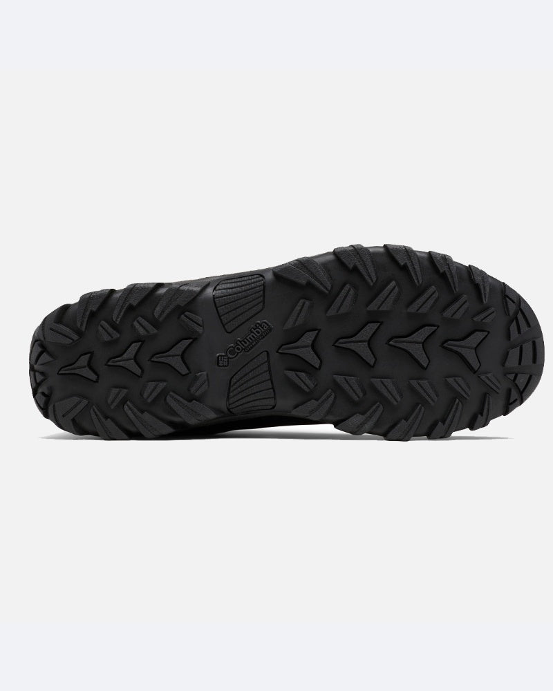 סולית הגומי השחורה של מגף הטיולים ColumbiaIL Buxton Peak Mid II, המוצגת מלמטה על רקע בהיר, כוללת חריצים מחוספסים רב-כיווניים המעניקים אחיזה והגנה מפני מים.