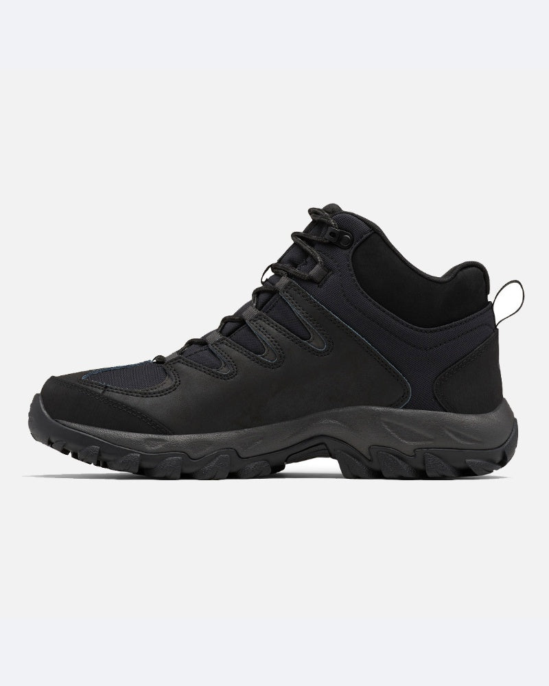 מגף טיולים שחור מדגם Columbia Il Buxton Peak Mid II, בעל סוליה עבה ומחוספסת, עיצוב אטום למים, סגירת שרוכים בחזית ותמיכה בקרסול, מוצג בפרופיל צדדי על רקע לבן חלק.