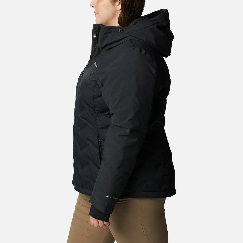 אדם המוצג בפרופיל לובש מעיל פוך שחור מדגם ColumbiaIL Grand Trek II עם ברדס וכיסים עם רוכסן, בשילוב עם מכנסיים בצבע חום בהיר, על רקע לבן חלק.