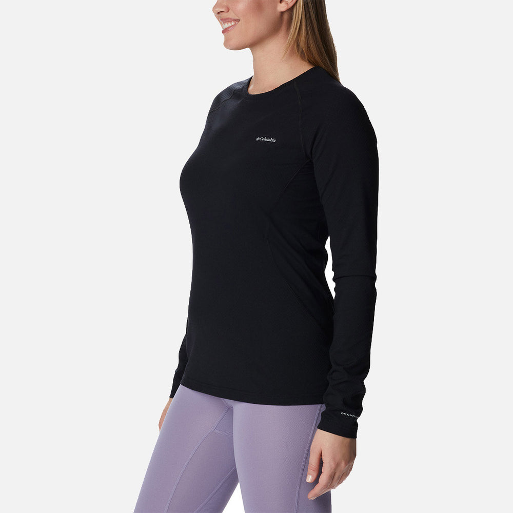 אישה הלובשת את חולצת ה-W Omni-Heat Infinity Knit L/S Crew של קולומביה IL בצבע שחור וטייץ בסגול בהיר עומדת בפרופיל, מחייכת על רקע לבן חלק.