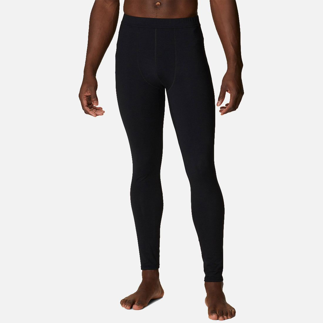 אדם עומד יחף, מדגמן את ה-Omni-Heat Infinity Tight M של ColumbiaIL — טייץ אימון שחור ומלוטש — המוצג מהכתפיים ועד כפות הרגליים על רקע לבן חלק.