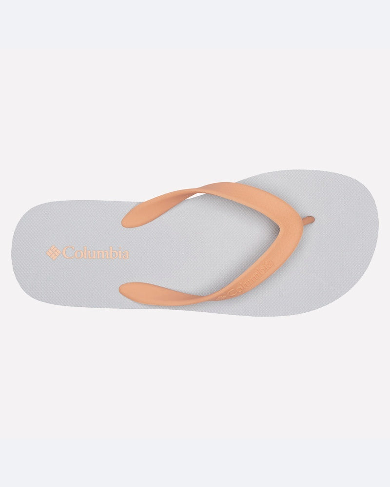 סנדל נשים Sun Trek Flip W של columbiaIL, עם סוליה בצבע אפור בהיר ורצועות בצבע אפרסק. לוגו columbiaIL מופיע בזהב על רפידת כף הרגל ליד העקב, על רקע לבן חלק.