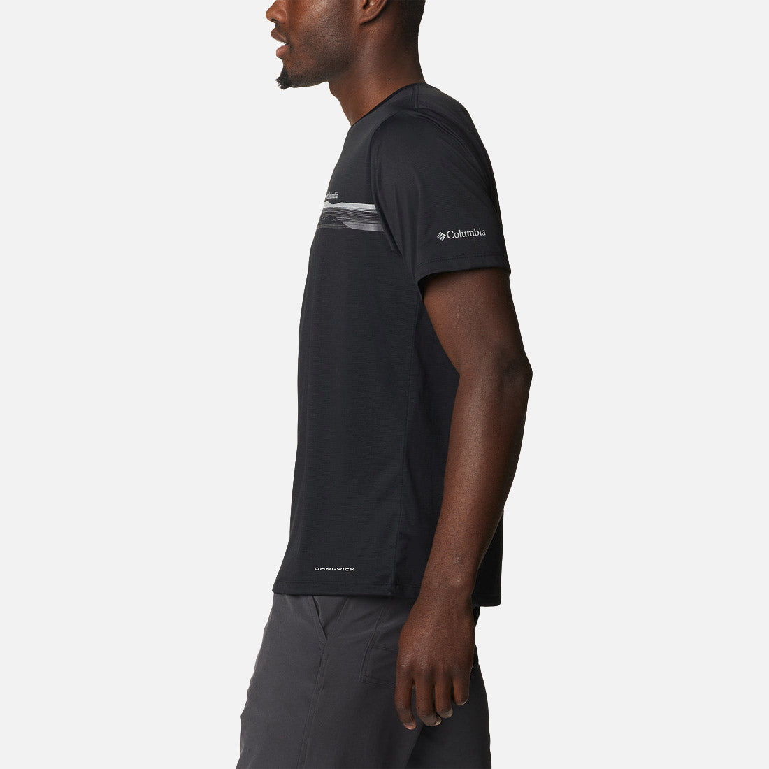 גבר עומד בפרופיל על רקע לבן, לבוש בחולצת Columbia Hike Graphic S/S T מבית columbiaIL — חולצת טיולים מסוגננת בשרוולים קצרים בצבע שחור, עם פסים אופקיים דקים ובהירים ולוגו קולומביה על השרוול.