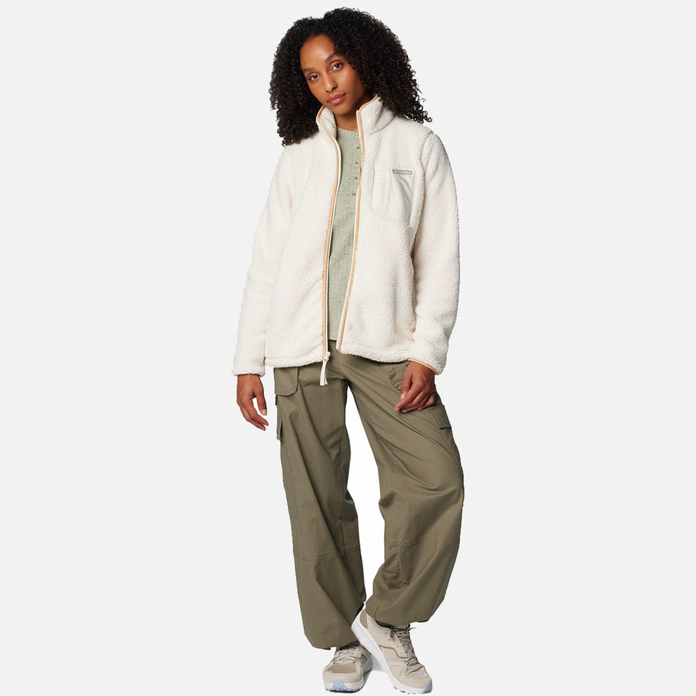 אישה עם שיער מתולתל לובשת מעיל לבן מדגם ColumbiaIL West Bend Full Zip II, חולצת הנלי בצבע ירוק בהיר, מכנסי קרגו רפויים בצבע זית ונעלי ספורט לבנות, כשהיא עומדת על רקע בהיר וחלק.