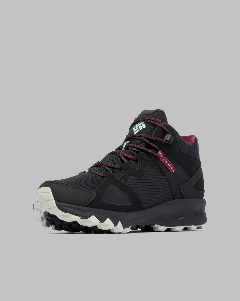 נעל הטיולים Peakfreak Hera Mid Outdry של קולומביה ישראל כוללת חלק עליון מרשת שחורה, שרוכים אדומים וסוליה לבנה ועמידה — אידיאלית לשימוש בשטח. מוצגת על רקע אפור אחיד.
