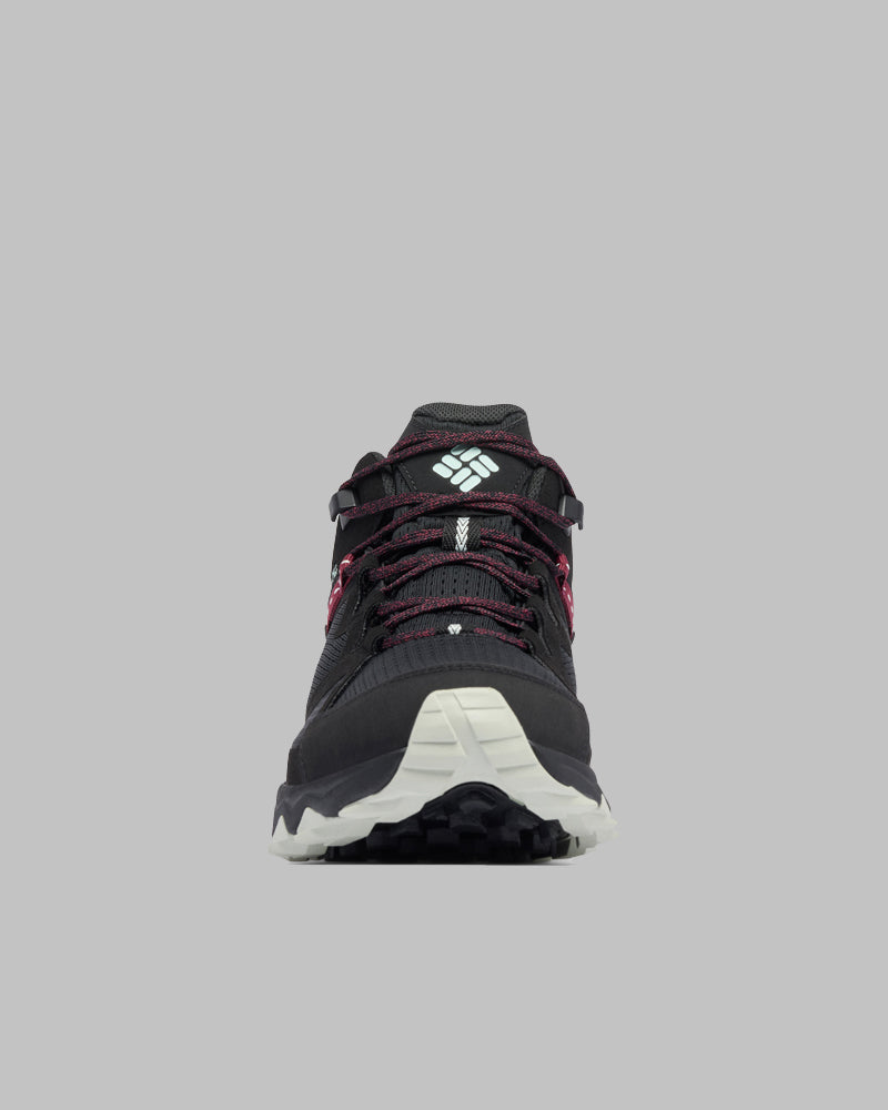 מבט מלפנים על נעלי הספורט "Peakfreak Hera Mid Outdry" של קולומביה ישראל בצבע שחור עם נגיעות של לבן וורוד, שרוכים לבנים וסוליה לבנה על רקע אפור אחיד — אידיאליות להרפתקאות אופנתיות בחיק הטבע.