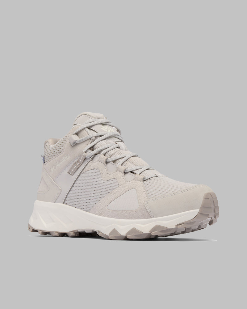 נעל הטיולים Peakfreak Hera Mid Outdry של קולומביה ישראל, בצבעי אפור בהיר ולבן, כוללת אלמנטים מרשת וזמש, סוליה עבה ודפוס סוליה מחוספס, כפי שנראית בזווית צד קדמית על רקע אפור אחיד.