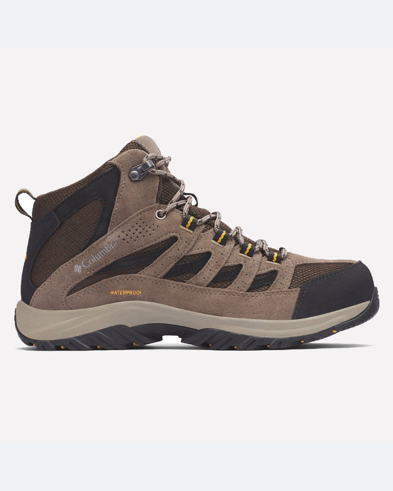 מבט צדדי על מגף "Crestwood Mid Waterproof" של המותג "columbiaIL" בצבעים חום ושחור עם נגיעות צהובות, לוחות רשת וזמש, סוליה עמידה ולולאות מתכת, על רקע לבן אחיד.