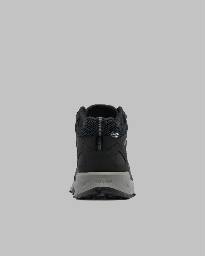 נעל הספורט Peakfreak II Mid Outdry M של ColumbiaIL, המוצגת בצבעים שחור ואפור במבט מאחור על רקע אפור, כוללת סוליה מרקמית, חלק עליון מרשת, לולאה בעקב וטכנולוגיית MID OUTDRY לשיפור הביצועים.